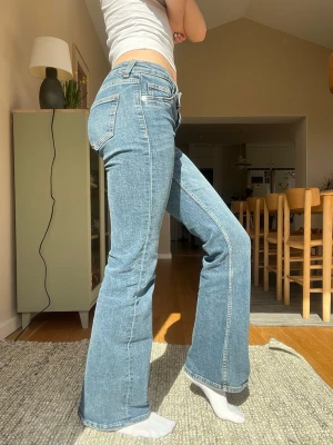 Blå bootcut jeans med låg midja - Snygga blå bootcut jeans med låg  midja och klassiska fem fickor. Jeansen har en ljus tvätt och raka, lätt utsvängda ben. Perfekta för en avslappnad och trendig look. Passar till både sneakers och boots.