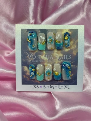 BlueDrift (S);Medin Square;Curved - Handgjorda press-on naglar i blå och turkosa toner med nude bas. Naglarna har handgjorda 3D-blommor och guldfärgade detaljer som snäckor och pärlor. Formen är medium square och i storlek S: 15 mm, 11,5 mm, 12 mm, 11 mm, 9 mm . Perfekt för dig som vill ha unika och kreativa naglar.