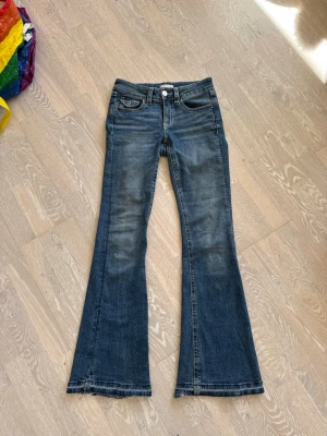 Blå lågmidjade bootcut jeans med fickdetaljer - Säljer ett par blå bootcut jeans med låg midja pch fickdetaljer. Jeansen har klassiska fem fickor, knappgylf och dekorativa sömmar på bakfickorna.  Säljer pga att jag inte använder längre de längre☺️ De var för korta för mig (173cm), så var tvungna att sprätta dem (se bild). Har annars inga synliga deffekter! 