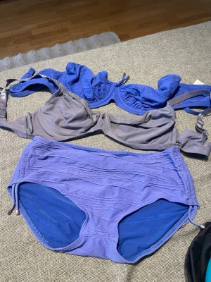 Blå och grå bikiniöverdel - Säljer en bikini i två delar, överdelen är blå och grå med bygel och justerbara axelband. Klassisk modell med enkel design, perfekt för stranden eller poolen. Materialet känns mjukt och följsamt mot huden. Trasigt spänne på blå toppen se bild, sitter en lösning som har funkat flera gånger