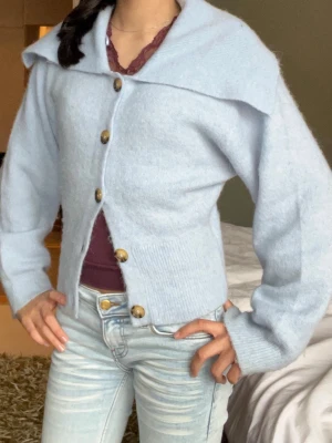 Ljusblå kofta från Gina Tricot - Superfin ljusblå kofta från Gina Tricot i ullblandning. Koftan har stora dekorativa knappar, bred krage och ribbade muddar. Perfekt att slänga över en topp för en chill och snygg look.