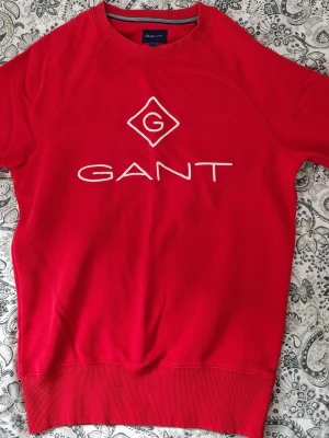 Röd sweatshirt från GANT - Tjena, säljer nu en riktigt snygg sweatshirt från GANT med stor vit logga och broderad detalj på bröstet. Den är väldigt skön och mjukt material. Den har en klassisk rund halsringning och ribbade muddar vid ärmslut och nederkant. Tveka inte att skriva vid några funderingar.