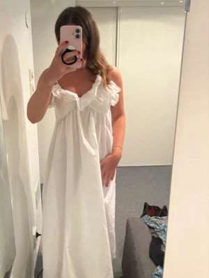 Vit långklänning med volang - Säljer en vit långklänning med volangdetaljer vid urringningen och axelbandslös design. Klänningen har en loose passform och är perfekt för sommarens varma dagar. Tillverkad i ett mjukt bomullstyg som känns luftigt och bekvämt.