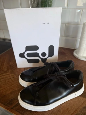 Eytys Doja sneakers - Säljer mina fina Eytys sneakers i modellen ”Doja Shiny Lace-up” i färgen ”Black Shiny Leather”❣️Du får med boxen! De är i fint skick men som visat på bild 6 så har lädret spruckit lite i fram på ena skon, men det är inget man tänker på! De är även lite slitna i bak som man även ser på bilderna, men det är inte heller så synligt när man har på sig skorna🌺