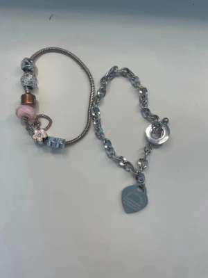 Två armband med berlocker och hjärthänge - Charm armband som går att öppna och lägga till flera charms. Armbandet är vatten tät förutom dem delen som man kan öppna armbandet.   Det andra armbandet har en bibel vers och är helt vatten tät