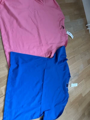 Två basic t-shirts i blått och rosa - Två stilrena t-shirts i bomull, en i klarblå och en i rosa. Båda har rund halsringning och korta ärmar. Perfekta för en enkel och clean look. Säljs tillsammans.