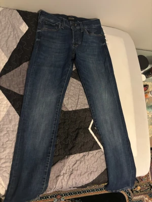 Mörkblå raka jeans - Säljer ett par mörkblå jeans med rak passform och klassisk femficksdesign. Jeansen har subtila slitningar och är tillverkade i denim med snygg tvätt. Perfekta för en avslappnad och stilren look.