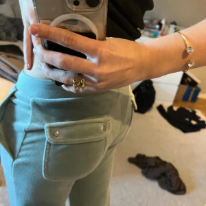 Mintgröna mjukisbyxor från Juicy Couture - Säljer ett par mintgröna mjukisbyxor från Juicy Couture i mjuk velour. Byxorna har raka ben, bred resår i midjan och fickor med lock och tryckknappar bak. Perfekta för en chill och trendig look.