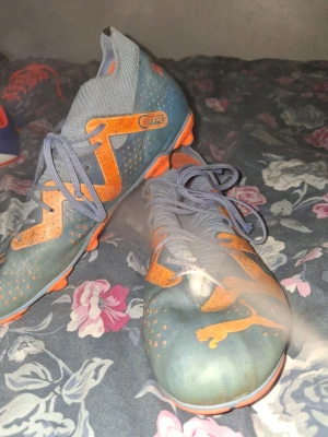 Blå-orange fotbollsskor från Puma - Säljer ett par snygga fotbollsskor från Puma i blått och orange. Skorna har en modern design med mönstrad ovandel, snörning och greppvänlig sula i orange. Perfekta för dig som vill sticka ut på planen och få bra kontroll på bollen.