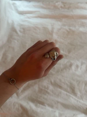 Chunky silverring med pärldetalj - Säljer en chunky silverfärgad ring med en unik, organisk form och en liten pärldetalj bredvid. Ringen har en modern och trendig design som sticker ut och passar perfekt för dig som gillar statement-smycken.