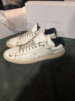  Oliver Cabell skor - Snygga vita sneakers från Oliver Cabell i äkta läder med grå snörning och svart detalj vid hälen. Klassisk låg modell med diskret logga på sidan och stilren design. Perfekta för dig som gillar minimalistisk och clean stil.