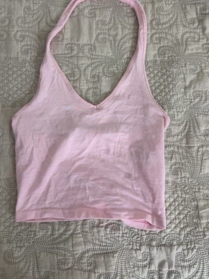 Ljusrosa croppad linnetopp - Säljer en ljusrosa croppad linnetopp med v-ringning och halterneck. Toppen är ärmlös och gjord i mjuk bomull, perfekt för varma dagar. Enkel och stilren design som passar till mycket.