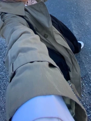 olivgrön trenchcoat Burberry - Säljer en klassisk beige trenchcoat från Burberry med bälte i midjan och typisk rutigt foder. Kappan har dubbelknäppning, axelklaffar och justerbara ärmslut. Perfekt för dig som vill ha en tidlös och ikonisk look.