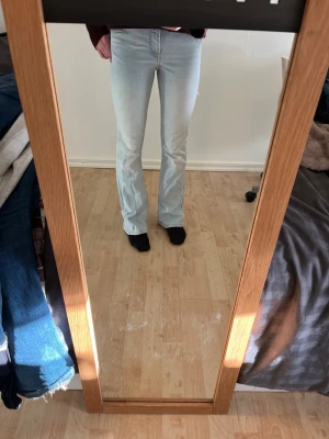 Ljusblå bootcut jeans - Säljer ett par ljusblå bootcut jeans med klassisk femficksdesign och hög midja. Jeansen har en snygg tvätt och är tillverkade i ett mjukt denimtyg som ger en bekväm passform. Perfekta för dig som gillar retrovibbar och vill ha ett par jeans som sticker ut.