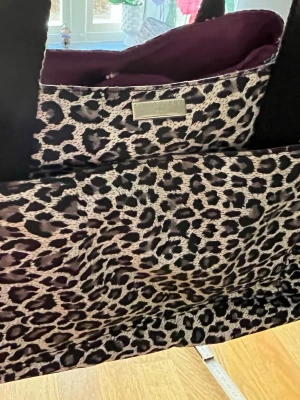 Leopardmönstrad väska från Sonia Rykeil - Snygg vintage väska från Sonia Rykeil Paris med leopardmönster i svart, beige och grå toner. Väskan har svarta axelband och lila innerfoder. Perfekt för dig som vill sticka ut med ett djurmönstrat statement-plagg.Har många fack.Mått finns på bilderna.Oanvänd