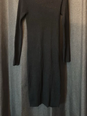 Svart glittrig långklänning - Snygg svart långklänning med diskret glittrigt material och lång ärm. Klänningen har en kroppsnära passform och är perfekt för dig som vill ha en stilren look med lite extra shine. Materialet känns mjukt och stretchigt.