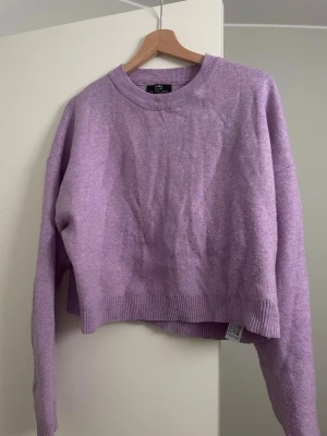 Ljuslila stickad tröja Bershka - Mysig ljuslila stickad tröja från Bershka med rund halsringning och ribbade muddar vid ärmslut och nederkant. Tröjan har en avslappnad passform och är perfekt för lager på lager. Materialet är mjukt och ger en skön känsla.