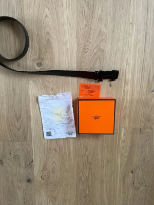 Svart Hm skärp med Hm -spänne - Snyggt svart skärp från Hm  med det ikoniska H-spännet i matchande svart. Skärpet är gjort i exklusivt skinn och kommer med originalbox och certifikat. Perfekt accessoar för att lyfta vilken outfit som helst.