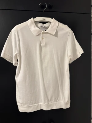 Vit pikétröja från Arket - Klassisk vit pikétröja från Zara med korta ärmar och krage. Tröjan har två knappar framtill och är gjord i mjuk bomull. Enkel och stilren design som passar till det mesta.