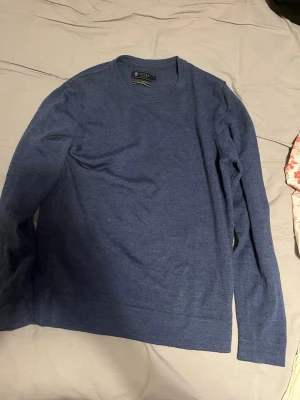 Blå stickad merino ull tröja från Riley - Mysig blå stickad tröja från Riley med rund halsringning och långa ärmar. Tröjan har en enkel och stilren design som passar perfekt till olika outfits. Materialet känns mjukt och bekvämt mot huden.