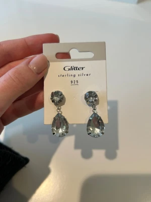 Silvriga droppformade örhängen - Snygga örhängen med stora, droppformade klara stenar. Örhängena har en klassisk och glittrig look med rund sten upptill och en större droppformad sten som hänger ned. Perfekta för dig som gillar statement-smycken. Använt skick därav priset!🙏🏻