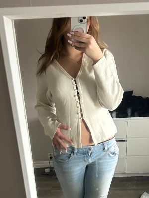 Krämvit tröja från Gina  -  krämvit tröja med unika knappar framtill och v-ringning. Långärmad modell i mjukt material som sitter snyggt i midjan. Inga teckan på användning.