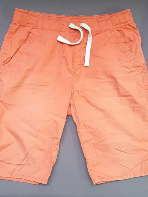 Orangea kortbyxor - Ca 76 cm midja. Aningen solblekta, några små hål i ena bakfickan och en permanent fläck där också. (Bild 3)