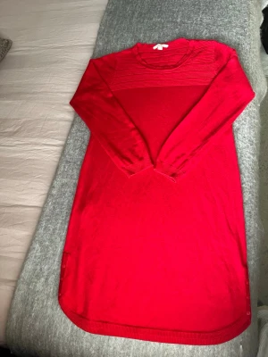 Röd långärmad stickad klänning - Snygg röd stickad klänning med rund halsringning och långa ärmar. Klänningen har en enkel, rak passform och ribbade detaljer upptill samt vid ärmslut och nederkant. Perfekt för dig som gillar en klassisk och bekväm stil.