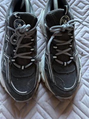 Grå chunky sneakers från Axel Arigato - Säljer ett par grå chunky sneakers från Axel Arigato med vita detaljer och tjock sula. Skorna har en sportig look med grå mocka och textil, samt vita och grå skosnören. Perfekta för dig som gillar streetwear och vill ha något som sticker ut. (Använt 1 gång) 