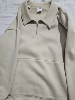 Beige halfzip hoodie från Selected Homme - Säljer en beige halfzip hoodie från Selected Homme. Tröjan har en hög krage med dragkedja och är gjord i mjukt, fleecefodrat material. Oversized fit och minimalistisk design utan tryck eller logga på framsidan. Perfekt för en chill och clean look. 