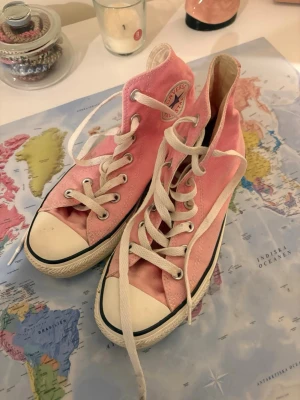 Rosa Converse All Star high tops - Säljer ett par klassiska Converse All Star high top sneakers i rosa med vita snören och tåhätta. Skorna har den ikoniska loggan på sidan och svart rand längs sulan. Perfekta för dig som vill ha en färgklick till din outfit.