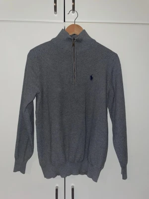Grå stickad tröja från Ralph Lauren - Snygg grå stickad tröja från Ralph Lauren med halv dragkedja och hög krage. 