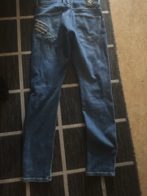 Blå slitna skinny jeans med hål Plein Sport - Säljer ett par blå skinny jeans med slitningar och hål på både fram- och baksida. Jeansen har klassisk femficksdesign och är tillverkade i denim. Perfekta för dig som gillar en trendig och avslappnad streetstil. Byxorna är äkta och priset kan diskuteras. S/M