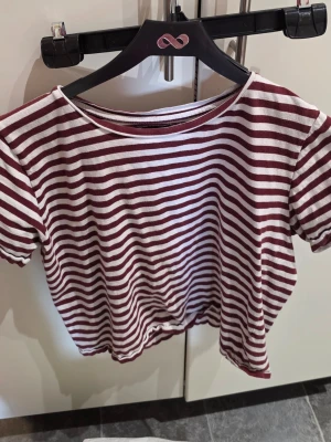 Randig t-shirt från 157, storlek S - Randig t-shirt från 157 i storlek S. T-shirten har vinröda och vita horisontella ränder, rund halsringning och korta ärmar. Perfekt för en avslappnad och trendig look. Materialet känns mjukt och skönt mot huden.