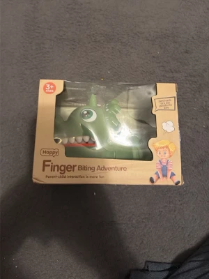 Finger Biting Adventure spel - Roligt spel för barn från 3 år och uppåt där man trycker på tänderna på en grön krokodil och hoppas att den inte biter. Perfekt för familjestunder och skratt. Levereras i originalförpackning.