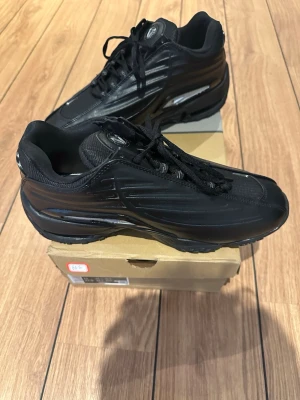 Nike skor  - Säljer ett par svarta skor sneakers med futuristisk design och glänsande detaljer. Skorna har en låg silhuett, svarta skosnören och en chunky sula. Materialet är en mix av syntet och mesh för bra komfort och stil.