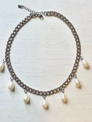 Kedjehalsband med pärldroppar - Snyggt halsband i silverfärgad metallkedja med sju hängande vita pärldroppar. Kedjan har justerbar längd och ger en cool kontrast mellan metall och pärlor. Perfekt accessoar för att lyfta din outfit.