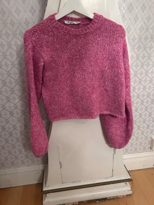 Rosa stickad tröja med öppen rygg NAKD - Trendig rosa stickad tröja från NA-KD med croppad passform och rund hals. Baksidan har en stor cut-out och knytband som ger en unik look. Perfekt för dig som vill sticka ut! Materialet är mjukt och mysigt, och tröjan har långa ärmar.