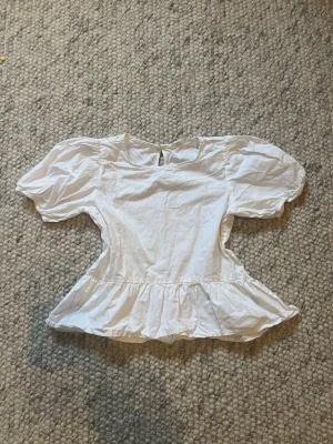 Sommar blus - Söt vit blus från H&M med puffärmar och volang nedtill. Blusen har rund halsringning och är tillverkad i bomull, vilket gör den lätt och bekväm. Perfekt för dig som gillar en feminin och trendig stil.💘
