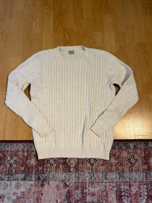 Vit kabelstickad tröja  - Kabelstickad tröja i mjuk vit färg. Klassisk rund halsringning och långa ärmar med ribbade muddar. Tröjan har ett stilrent mönster och är perfekt för dig som gillar en clean och tidlös look.
