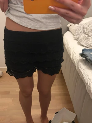 Svarta spetsiga shorts med volang - Säljer ett par svarta shorts med bred resår i midjan och flera lager volang i spets. De har en feminin look med snygg struktur och passar perfekt till sommaren. Supersköna och lätta att matcha med olika toppar.