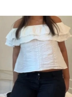 Vit offshoulder volangtopp - Superfin vit offshoulder topp med volangdetaljer och bred resår upptill. Toppen är croppad och har en luftig passform, perfekt för varma dagar. Materialet känns som bomull och ger en lätt och fräsch känsla.