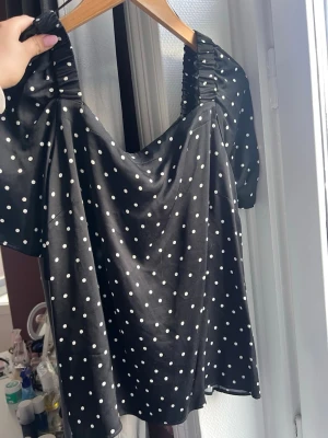 Svart prickig topp från STOCKH LM - Snygg svart topp från STOCKH LM med vita prickar och puffiga korta ärmar. Toppen har en lätt rynkad detalj vid axlarna och en luftig passform. Perfekt för dig som gillar en trendig stil.  Lite ”riv” märke framtill men ingen större defekt.