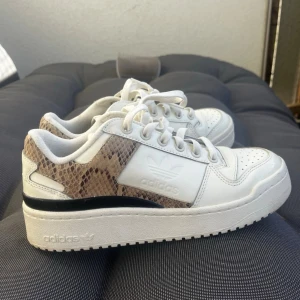 Adidas Forum Bold W White Black Snakeskin - Säljer ett par riktigt snygga vita sneakers från Adidas med beige/bruna snake-detaljer som ger en exklusiv touch 🐍✨   Perfekta till både vardag och lite mer uppklädda outfits. Superbekväma och lätta att matcha med allt från jeans till klänning 👌 Strl 38 2/3  