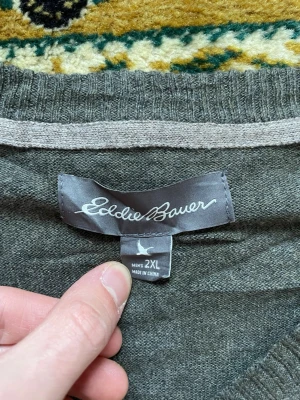 Grå tröja från Eddie Bauer 2XL - Mjuk och stilren grå tröja från Eddie Bauer i storlek 2XL. Tröjan har V-ringning och långa ärmar, perfekt för lager på lager eller som den är. Passar dig som gillar en enkel och klassisk look.