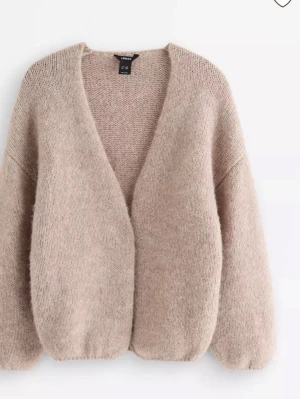 Beige stickad kofta från Lindex - Mysig beige stickad kofta från Lindex med öppen front och avslappnad passform. Koftan har långa ärmar och är tillverkad i ett mjukt, fluffigt material som passar perfekt för lager-på-lager-stil.