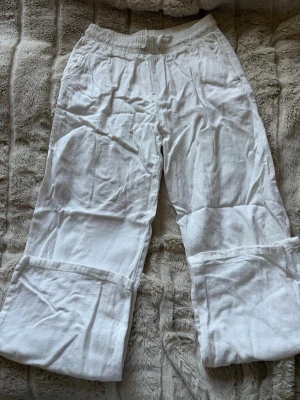Vita linnebyxor från Lindex - Säljer ett par vita linnebyxor från Lindex med resår i midjan och raka ben. Byxorna har fickor på sidorna och är tillverkade i ett luftigt linnematerial, perfekta för varma dagar. Passar dig som gillar en avslappnad och enkel stil.