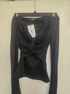 Svart omlottopp från BikBok - Supersnygg svart omlottopp från BikBok med lång ärm och cool twistad detalj framtill. Toppen har en djup v-ringning och är gjord i ett mjukt, stretchigt material som sitter riktigt snyggt på kroppen.