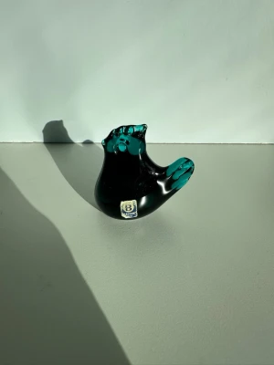 Blå glasfågel från Bergdala - Unik blå glasfågel från Bergdala glasbruk. Fågeln är handgjord i tjockt glas med en djupblå / turkos färg och transparenta detaljer på vingar och huvud. Perfekt som dekoration eller samlarobjekt. Märke sitter kvar på framsidan. Ca 7cm. Fint skick!