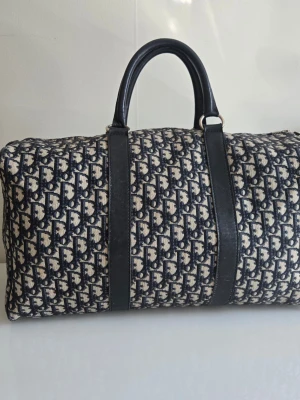 CHRISTIAN DIOR Speedy Weekend Bag - CHRISTIAN DIOR. Väska, modell “Speedy” weekend bag, med ikoniskt monogrammönster samt läderdetaljer. Tillverkad i Frankrike. Elegant och tidlös modell med klassisk Dior-design. Perfekt som weekendväska, handbagage eller vardagsbruk. Mått: ca 46 × 25 × 22 cm Mindre märken invändigt och på detaljer, men i gott bruksskick och fullt funktionell. En stilren vintageväska från Dior som håller länge och passar alla tillfällen.